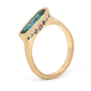 Gold ring with green and purple gemstones on a white background