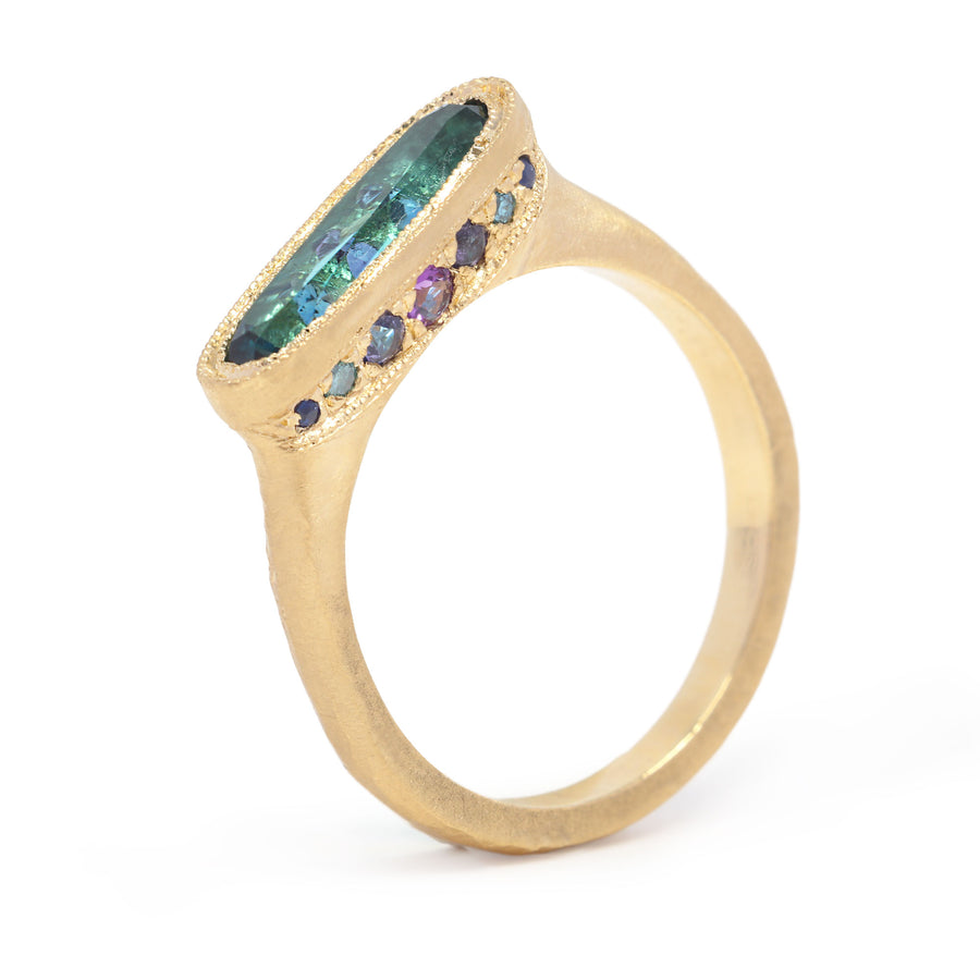 Gold ring with green and purple gemstones on a white background