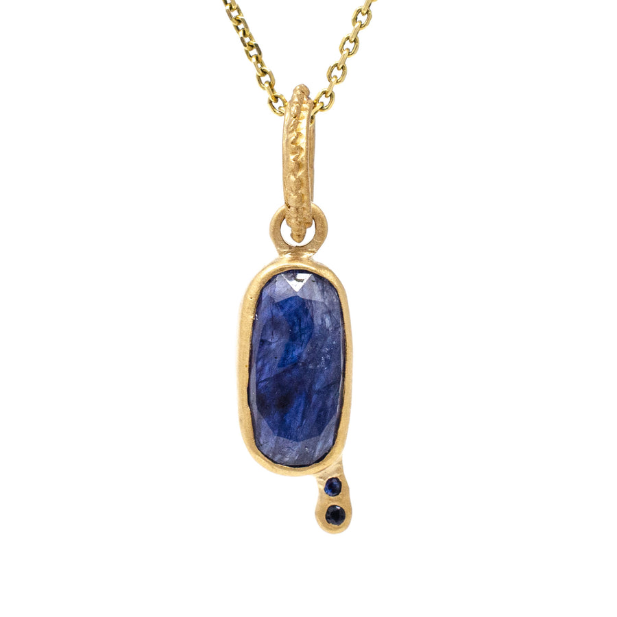 A blue sapphire charm pendant with two round cut blue sapphires, in 14k yellow gold.