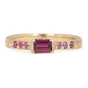 Gold ring with a central red gemstone and smaller pink stones on a white background