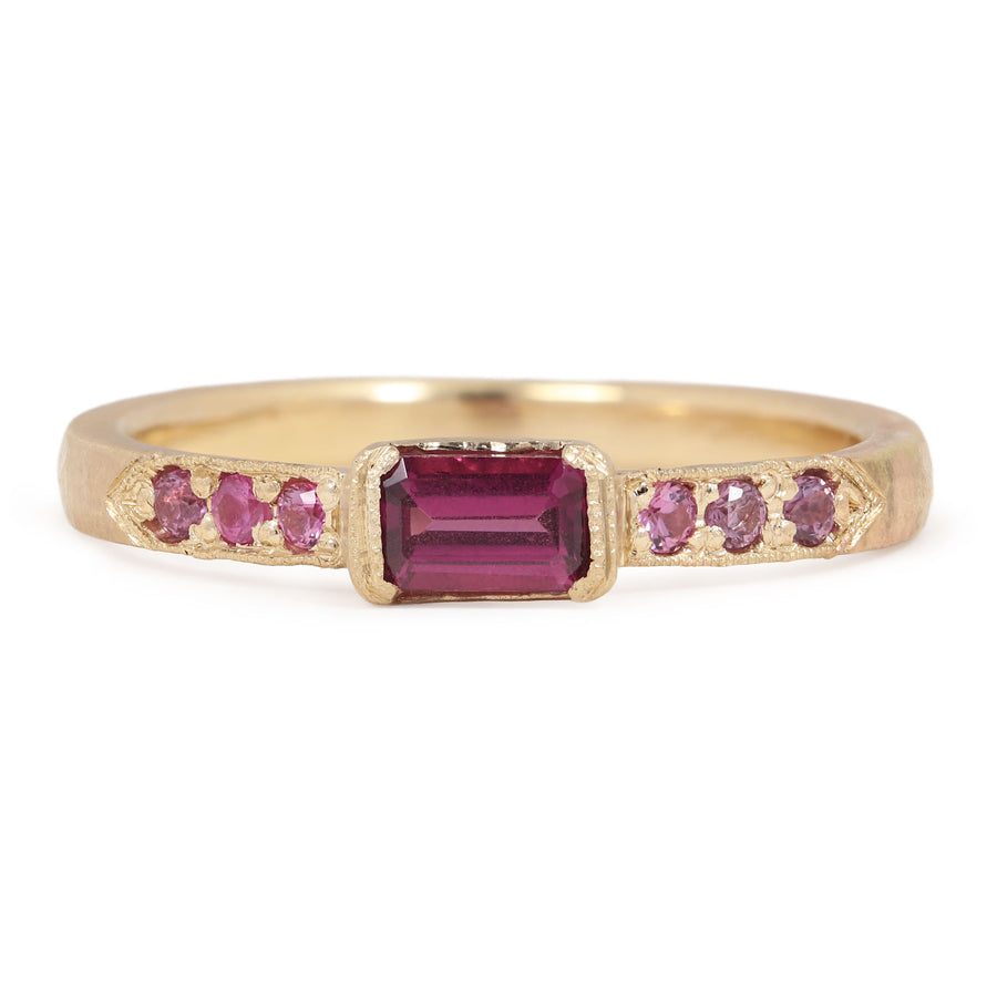 Gold ring with a central red gemstone and smaller pink stones on a white background